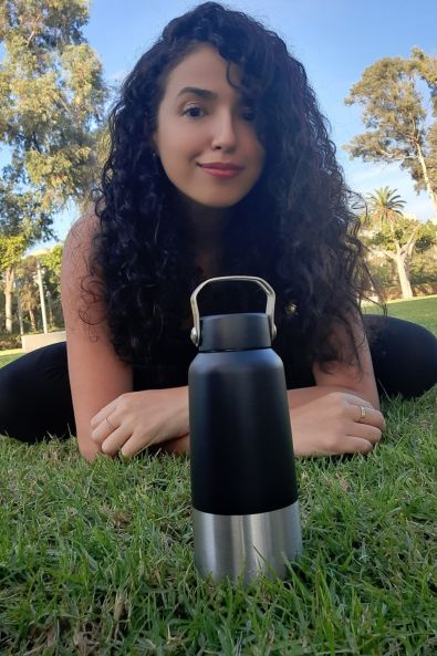 Femme assise sur le gazon devant elle une bouteille d'eau réutilisable en inox