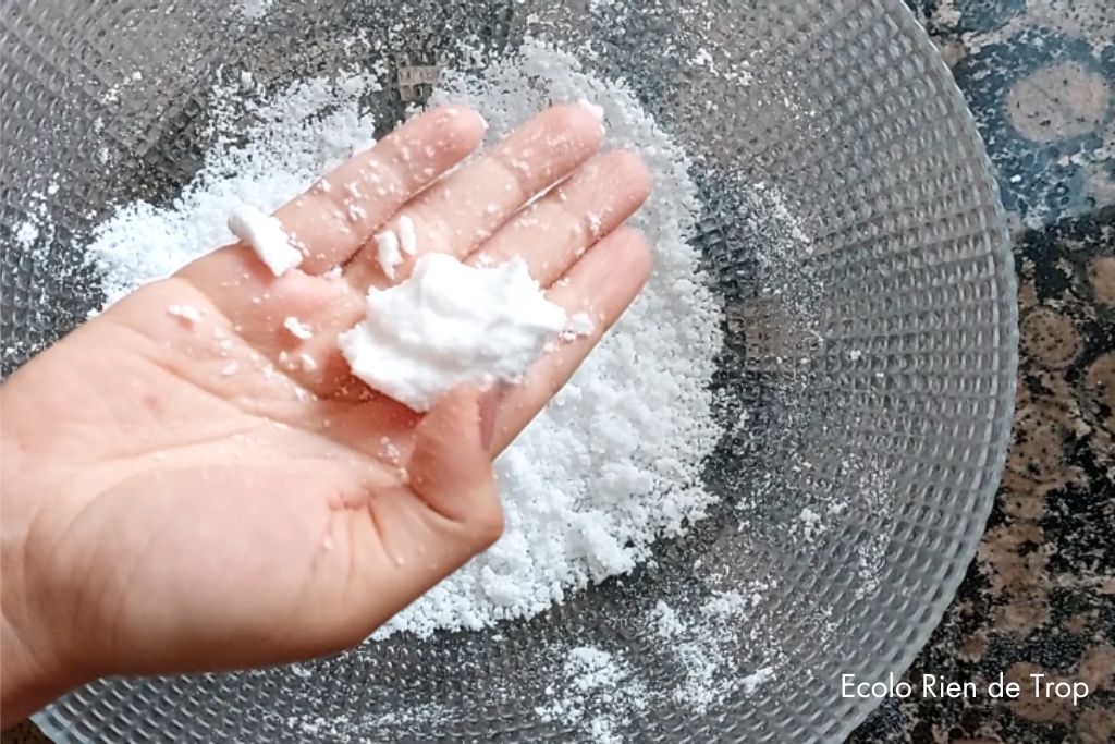 Main remplie d'une boule formée à partir des ingrédients dans le récipient en verre qui montre comment faire les bombes nettoyantes zéro déchet 